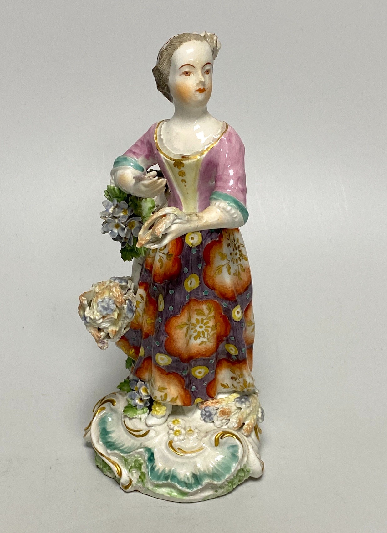 A Derby porcelain figure, emblematic of Summer, modelled as a woman wearing a floral patterned skirt and holding a sheaf of corn, patch marks and red anchor mark, 18th century, 19cm high